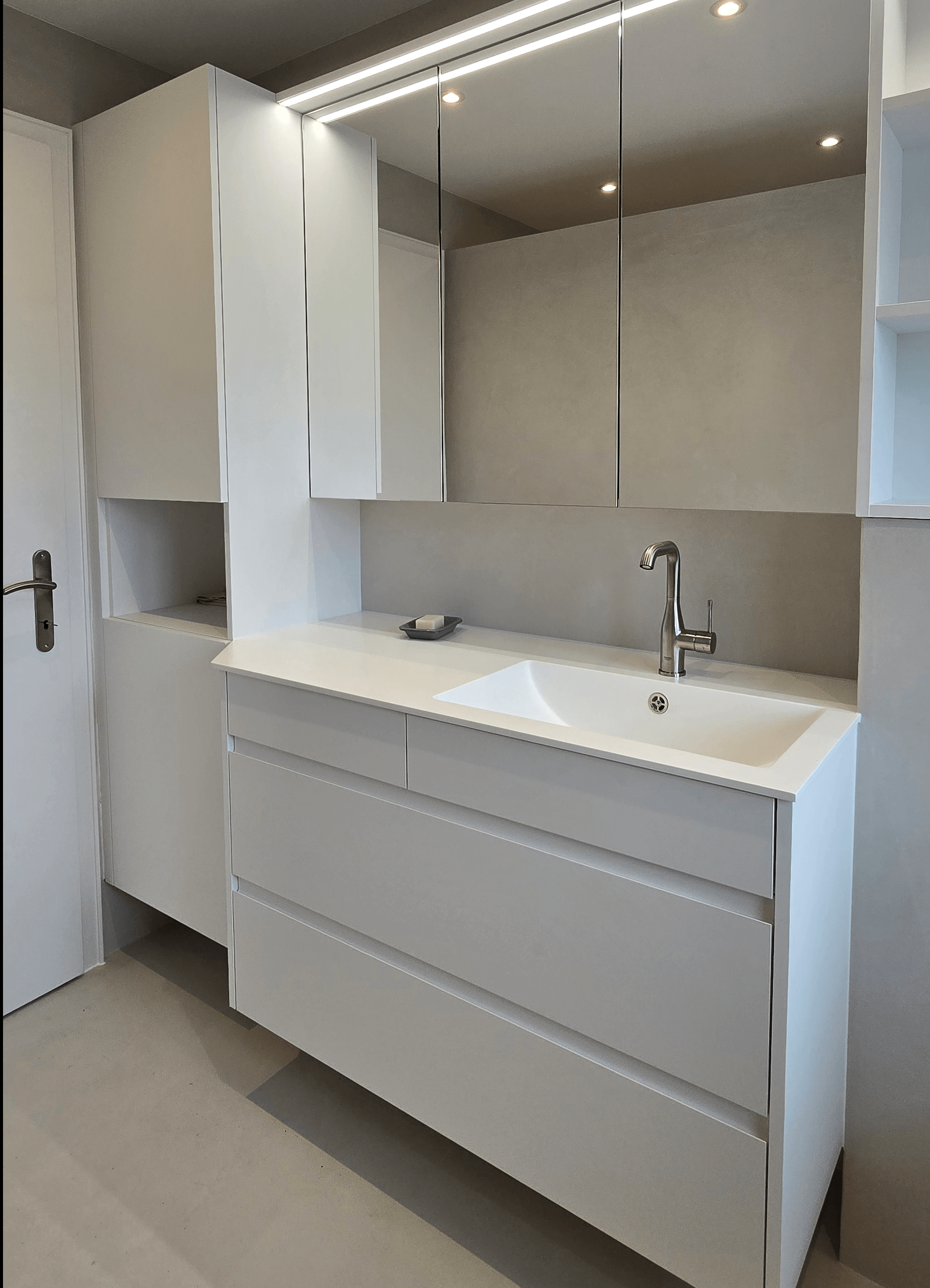 Badezimmer-Moebel in weiss matt, grifflos, weisse Kompaktplatte als Arbeitsplatte, edler Wasserhahn, Spiegelfronten, offene Regale