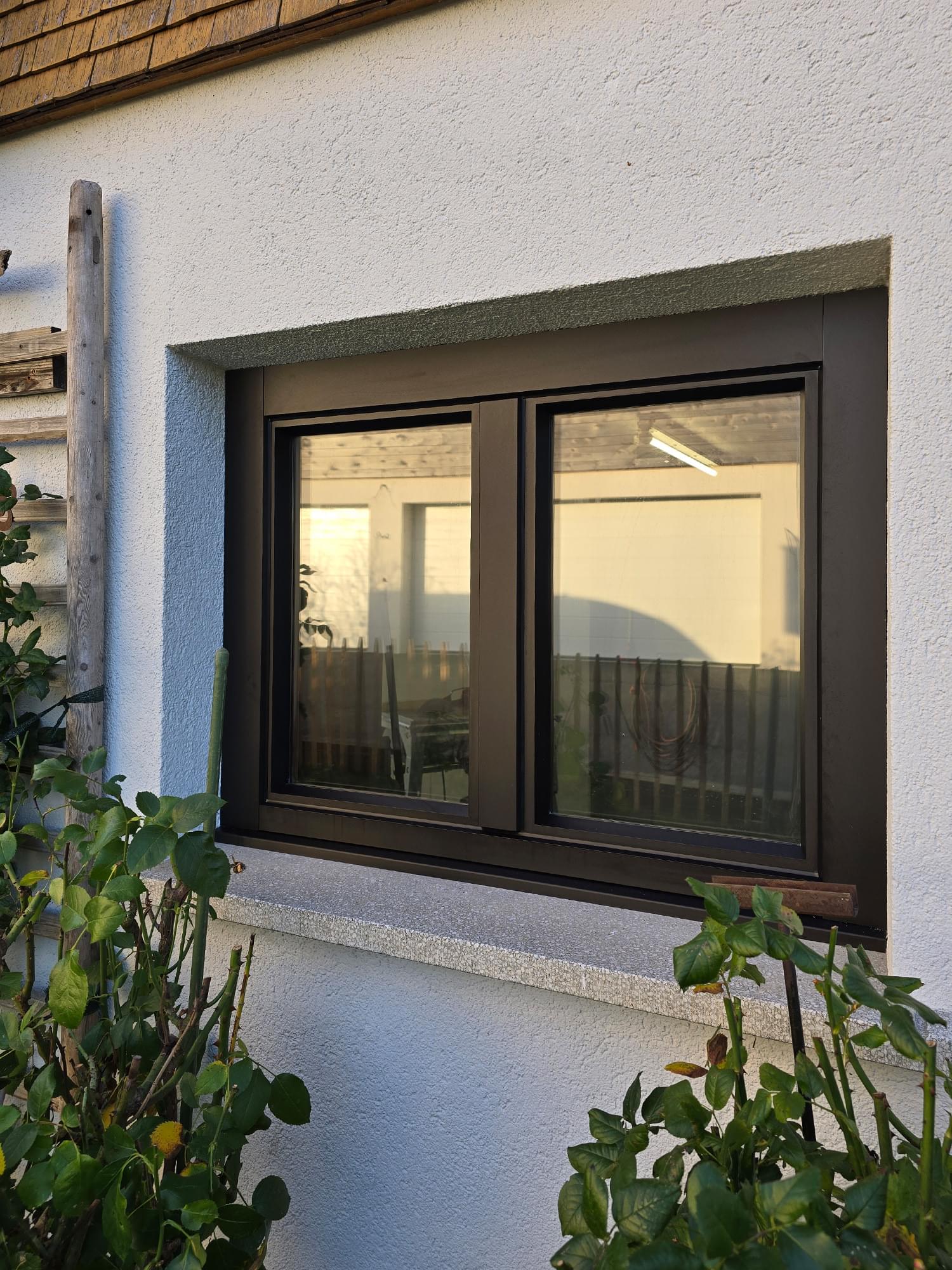 Frisch renoviertes Fenster mit schwarzem Alurahmen vor weißem Putz